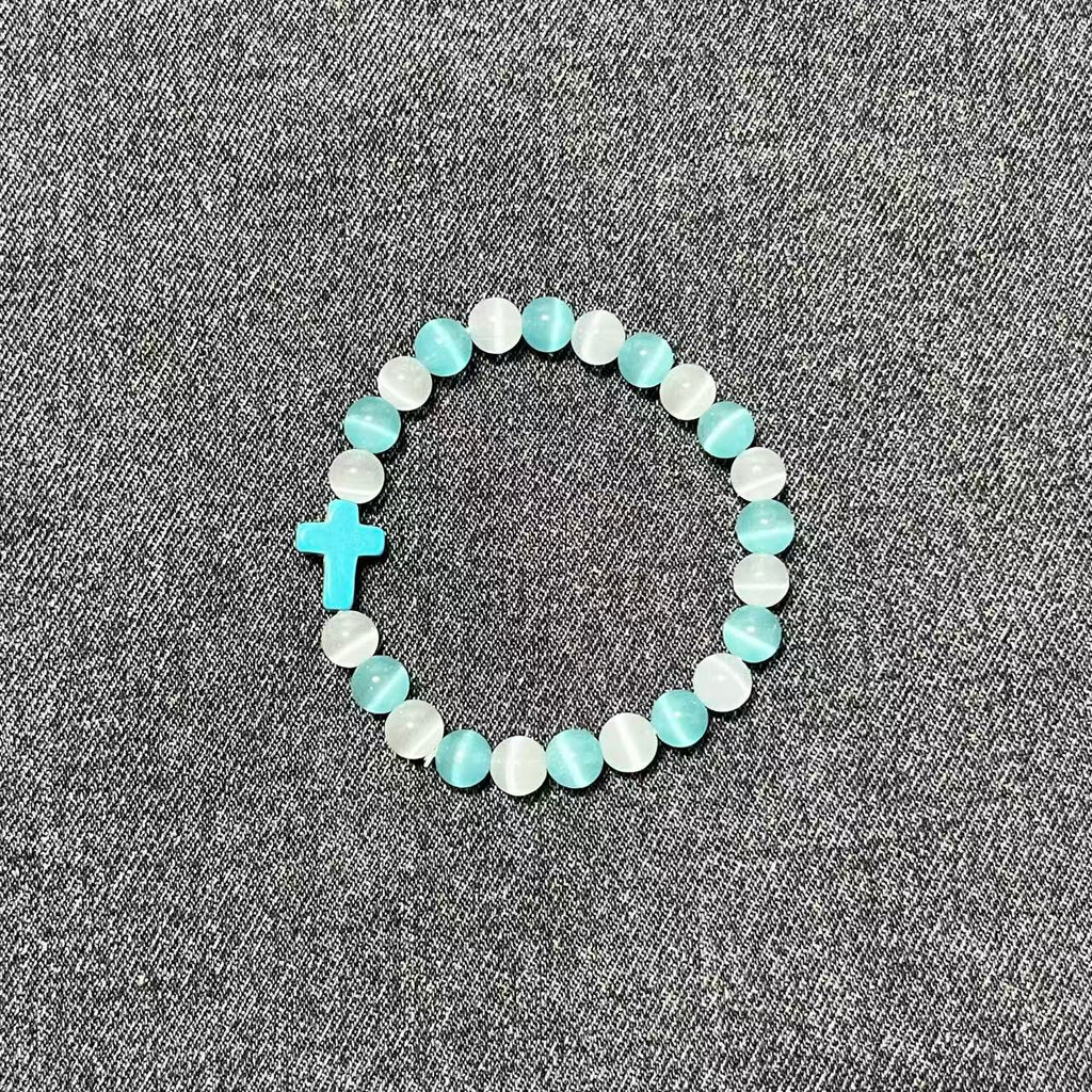 A single Aether Cross beaded bracelet made of alternating white and light blue chatoyant cat-eye crystals with a turquoise sacred cross charm.