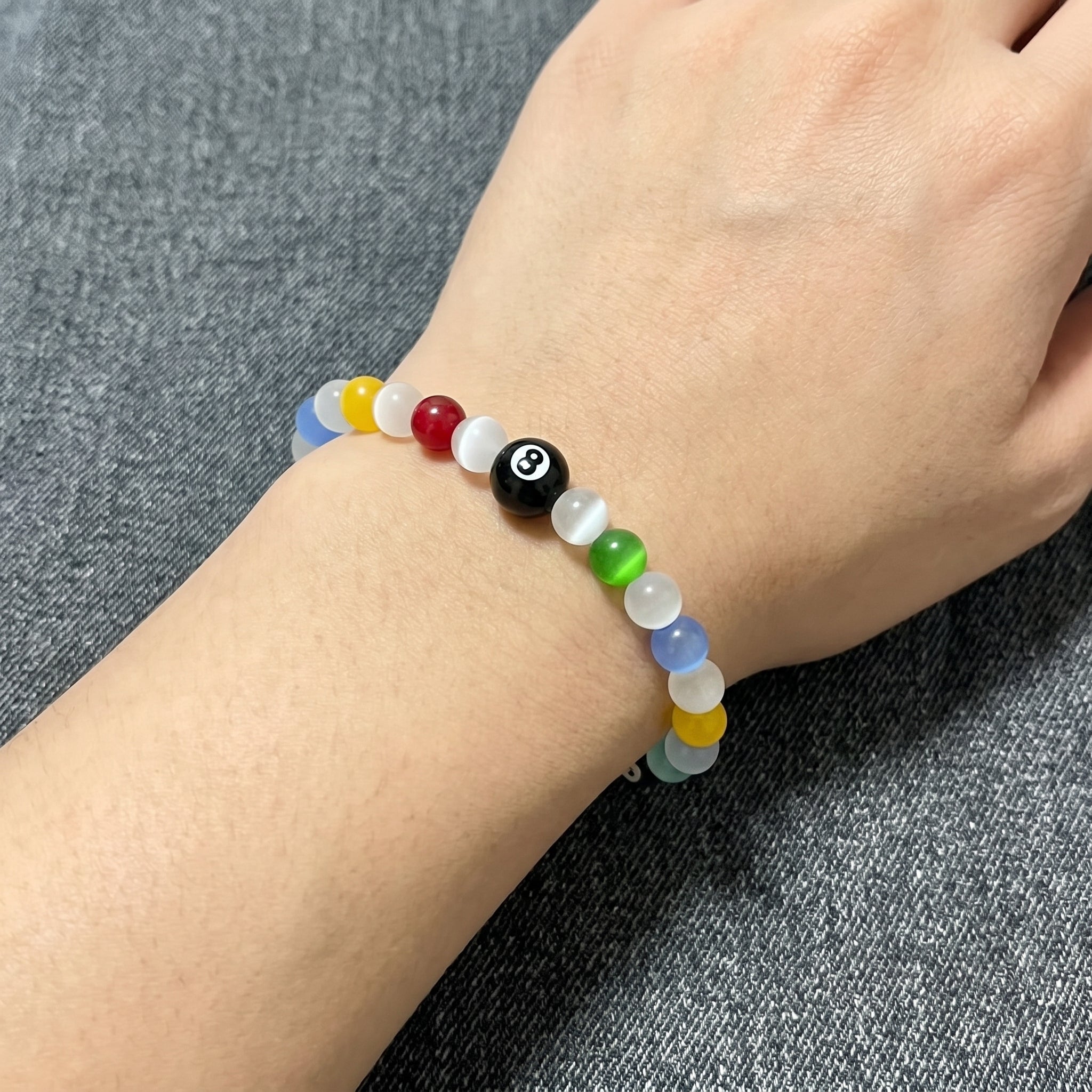 Close-up of a person wearing the SpiritPalette Chroma Rebel rainbow cat-eye crystal bracelet on their wrist, styled with a denim shirt at a wooden outdoor table.