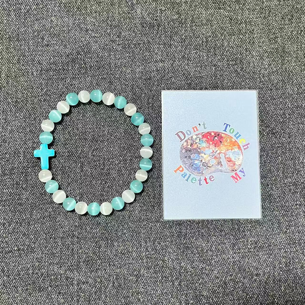 Cyan and white crystal beaded protection bracelet next to SpiritPalette art label on textured gray denim fabric.